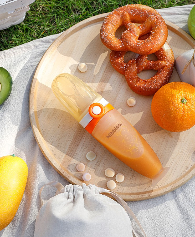 Nibbles silicone spoon feeder in orange and white, filled with baby food.