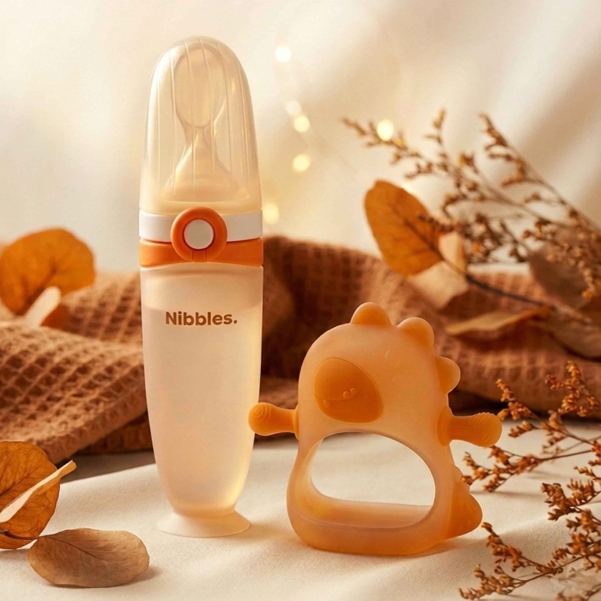 Nibbles silicone spoon feeder and dino teether set on a soft neutral autumn background